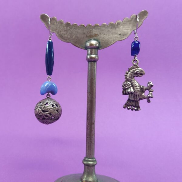 Dormeuses asymétriques argentées composées de perles bleues en verre et en plastique  d'une créature fantastique en métal argenté et d'une perle asiatique finement ciselée en argent.