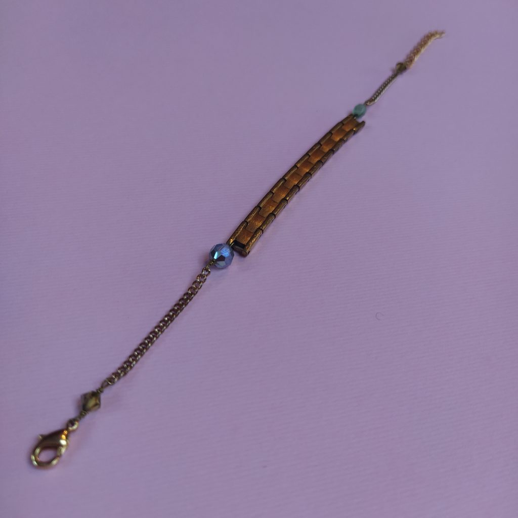 Bracelet comportant un bout d'ancien bracelet de montre métallique  diverses chaînes dorées et des perles de verre.