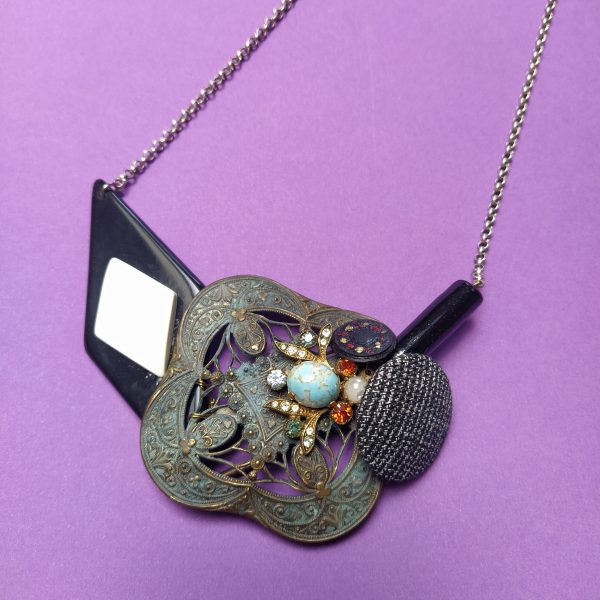 Plastron composé d'une ancienne broche  d'une antique buocle de ceinture  d'un clip d'oreille  de 2 boutons rétro et d'une grande perle de verre noire.