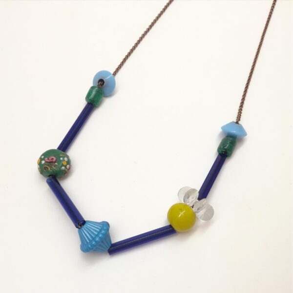 Collier de 76cm de longueur composé de tubes de verres et de perles de formes diverses et variées en couleurs  formes et matières. Couleur dominante : bleu.