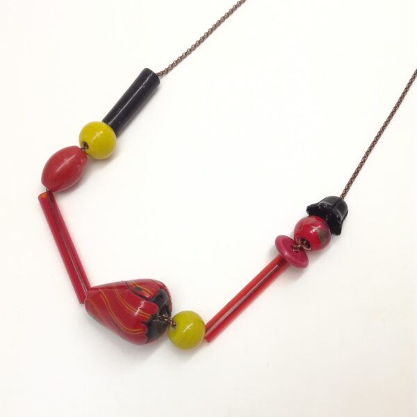 Collier de 76cm de longueur composé de tubes de verres et de perles de formes diverses et variées en couleurs  formes et matières. Couleur dominante : rouge.