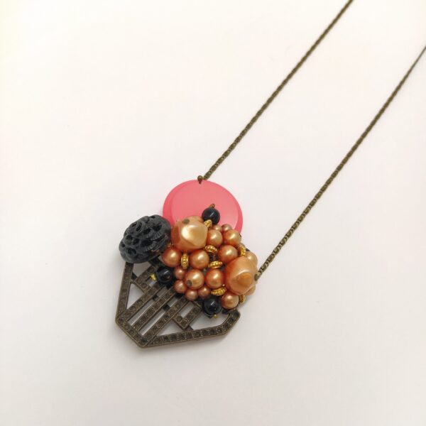 Sautoir en laiton bronze composé d'un élément de boucle de ceinture Art Déco  d'un clip vintage composé de perles nacrées orangées  d'un bouton de verre des années 1930 et d'un bouton des années 1980 rose fluo.
