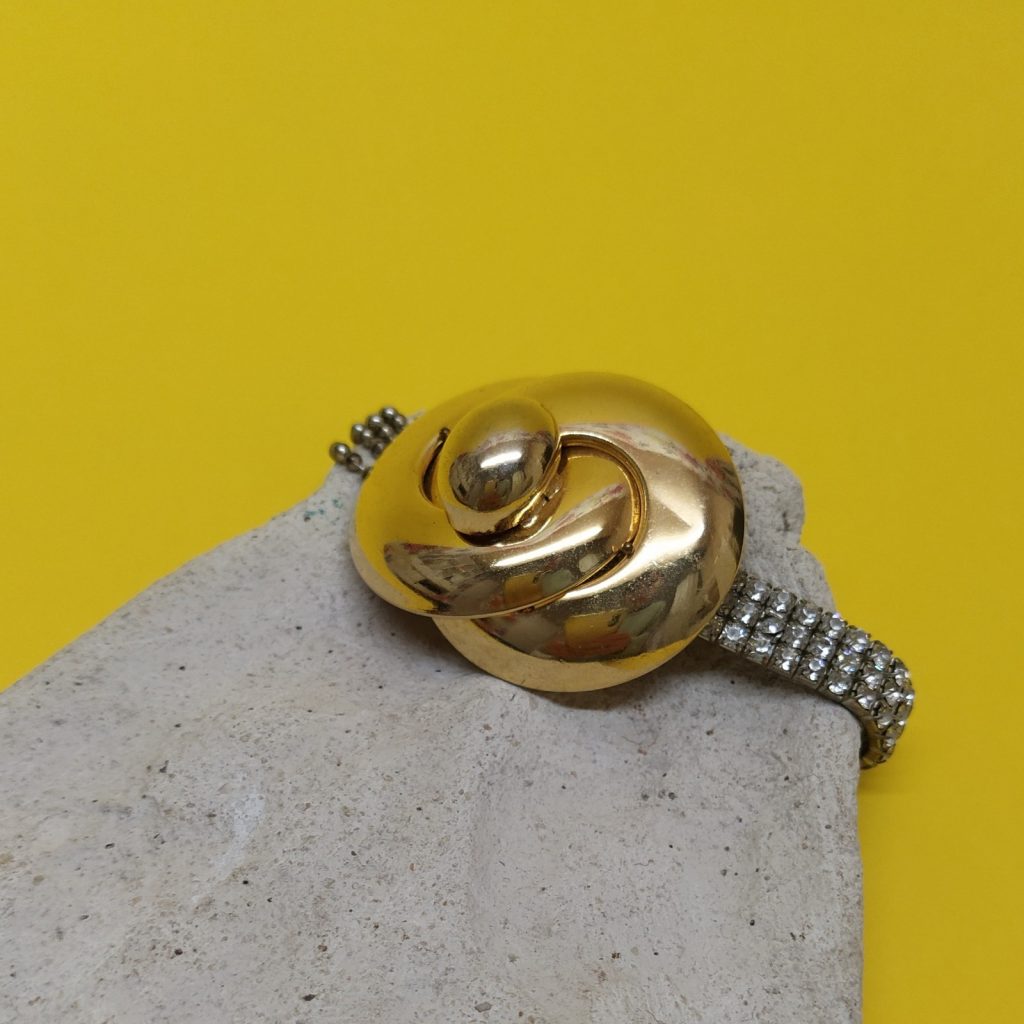 Bracelet extensible composé de strass et de chaînes boule argentée surmonté d'un clip vintage doré des années 1980.